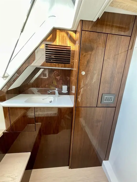 Modern yacht interior featuring a compact kitchen area with sink, cabinets, and a control panel. Bright, polished wood finish.